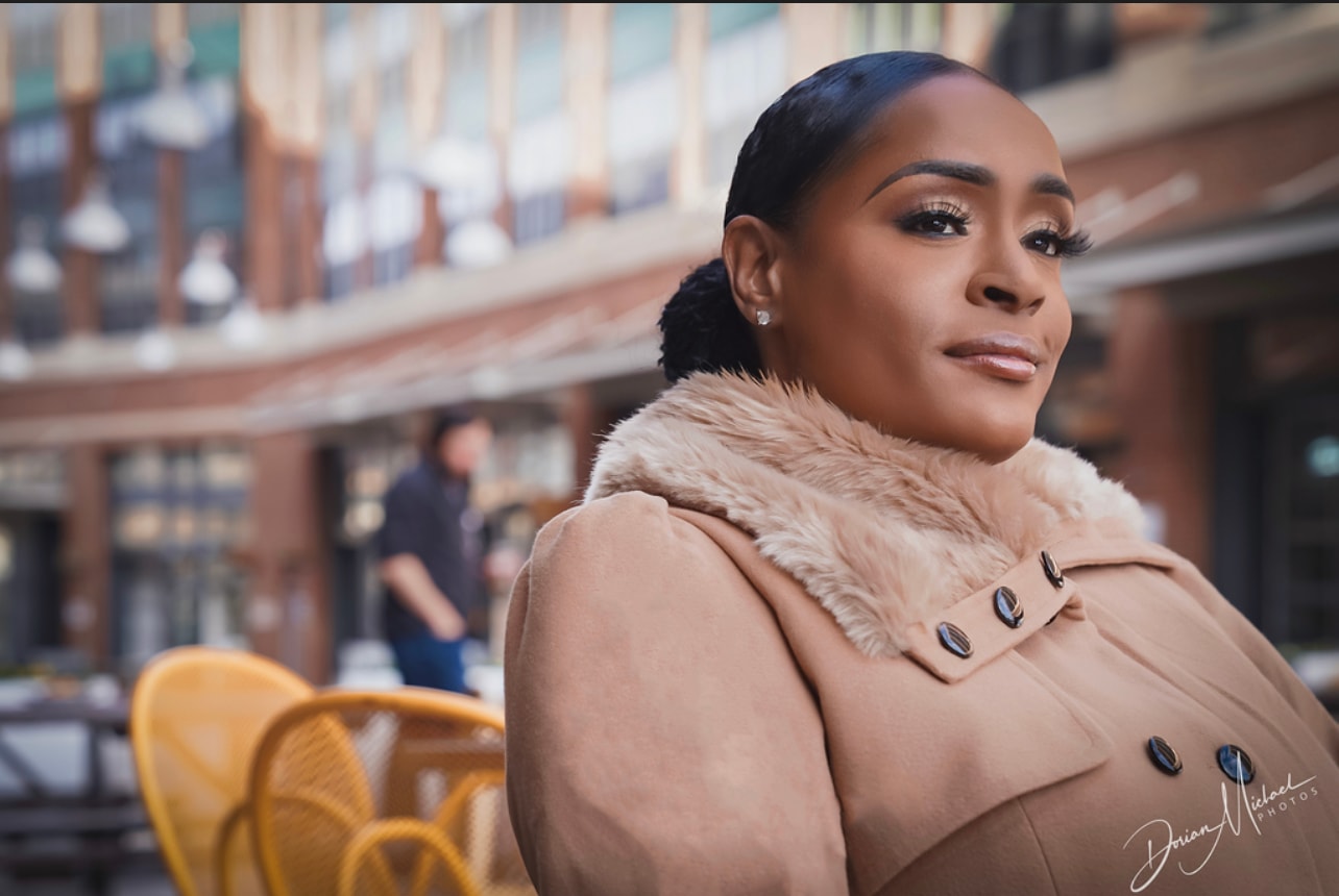 Aubree Bravo — camel coat, orange turtleneck, side profile